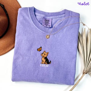 Folded VIOLET Comfort Colors shirt with cute Yorkshire Terrier puppy and butterfly graphic, personalized dog lover tee with custom pet name, minimalist pet shirt flat lay aesthetic gift idea.