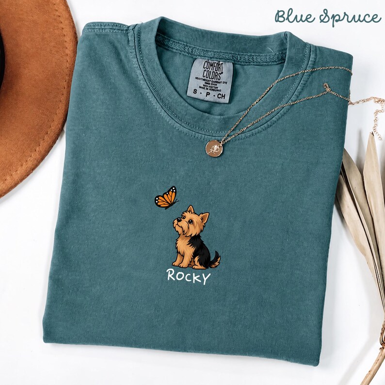 Folded BLUE SPRUCE Comfort Colors shirt with cute Yorkshire Terrier puppy and butterfly graphic, personalized dog lover tee with custom pet name, minimalist pet shirt flat lay aesthetic gift idea.
