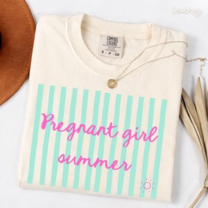 Ivory Comfort Colors shirt with vertical mint green stripes and pink script text reading “Pregnant girl summer” centered across the front, with a small pink sun icon detail at the bottom corner.