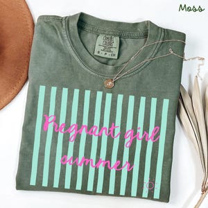 moss Comfort Colors shirt with vertical mint green stripes and pink script text reading “Pregnant girl summer” centered across the front, with a small pink sun icon detail at the bottom corner.