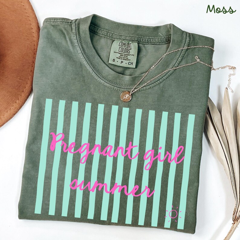 moss Comfort Colors shirt with vertical mint green stripes and pink script text reading “Pregnant girl summer” centered across the front, with a small pink sun icon detail at the bottom corner.