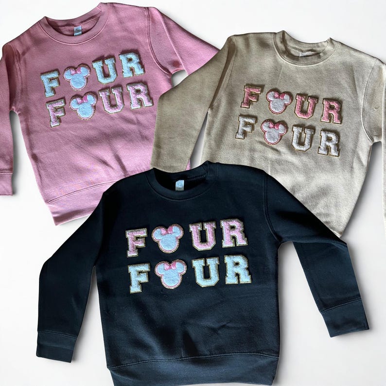 K&ouml;nnte beinhalten: Drei Sweatshirts mit Rundhalsausschnitt in Rosa, Beige und Schwarz. Jedes Sweatshirt zeigt das Wort "FOUR" in einem Blockbuchstabenstil mit einem Mickey Mouse-Kopf in der Mitte. Die Buchstaben und M&auml;usek&ouml;pfe sind in einer Kontrastfarbe gehalten.