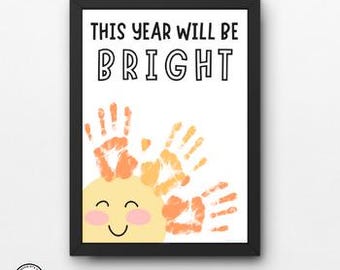 May include: A printable art print with the text "This year will be bright" and a yellow sun with orange handprints around it.