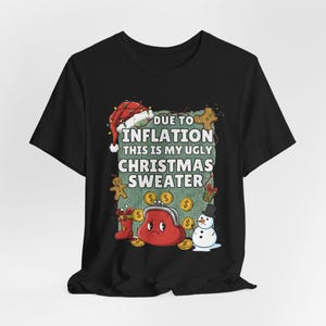 May include: Black t-shirt featuring a festive Christmas design. The design includes a Santa hat, a red purse, coins, and the text "Due to Inflation, This Is My Ugly Christmas Sweater."