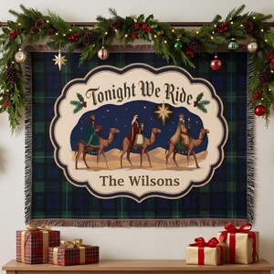 May include: A rectangular woven tapestry featuring a dark green and blue plaid pattern. The centre displays a cream-coloured scalloped emblem with the text Tonight We Ride and The Wilsons, depicting three figures riding camels under a star.
