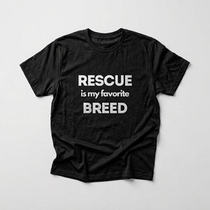 May include: A black short-sleeved t-shirt featuring white text printed on the chest. The text reads RESCUE is my favorite BREED in a bold, sans-serif font. The garment has a classic crew neckline and a standard fit with short sleeves.