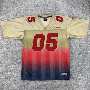May include: A short-sleeve V-neck jersey in beige, red, and dark blue with a vertical gradient pattern. The front features the large red number 05, the text FUBU, and a small patch with the number 05. The number 5 and 0 are on the shoulders.