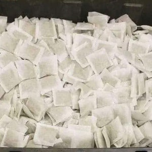 Könnte beinhalten: Eine große Menge weißer Teebeutel sind in einem Metallbehälter gestapelt.