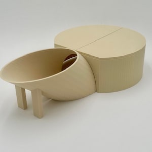 May include: A beige 3D printed model of a house with a curved roof and a separate cylindrical structure. The house has a small opening on the side and two legs.