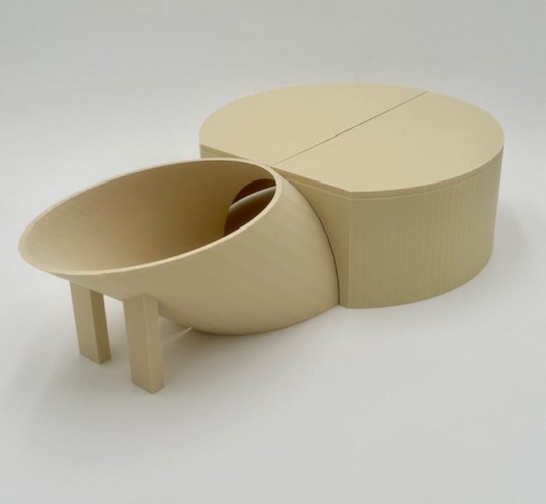 May include: A beige 3D printed model of a house with a curved roof and a separate cylindrical structure. The house has a small opening on the side and two legs.