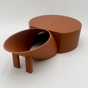 May include: A terracotta-colored ceramic object with a rounded top and a curved, hollow section with two legs. The object is made of two pieces that fit together.