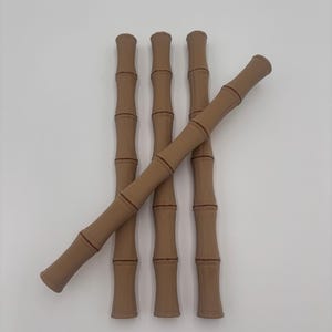 May include: Five bamboo-shaped decorative items. The items are a light brown colour with darker brown accents at the joints. One item is angled across the others. The items are arranged against a white background.