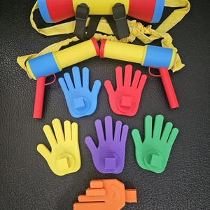 Puede incluir: Un conjunto de accesorios de juguete que incluye un depósito tipo mochila en amarillo, rojo y azul, dos pistolas de mano a juego y seis accesorios coloridos con forma de mano en azul, rojo, amarillo, morado, verde y naranja con conectores cuadrados.