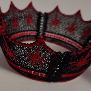 May include: A black and red lace crown with a spiderweb design. The crown is made of delicate lace and has a pointed top.