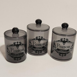 May include: Three grey apothecary jars with black lids. Each jar has a label with the word "Poison" and a skull design. The labels also include the names "Strychnine" and "Arsenic".