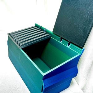 May include: A green and blue plastic storage box with a black lid. The lid has a series of ridges on the inside.