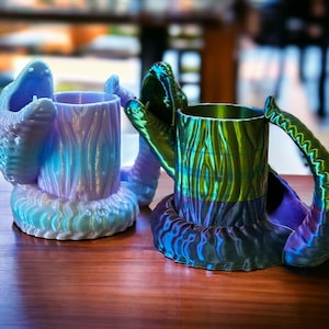 May include: Two 3D printed mugs with a wood grain pattern. The mug on the left is light blue and the mug on the right is green and purple.