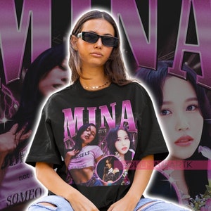 May include: A black t-shirt with a pink graphic print of a woman with the word "MINA" in large pink letters. The graphic also includes the words "Yourself" and "Someone" in smaller white letters.