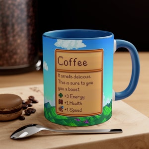 May include: A blue and white coffee mug featuring a pixelated design of a video game item called "Coffee". The text reads "It smells delicious. This is sure to give you a boost. +3 Energy +1 Health +1 Speed"