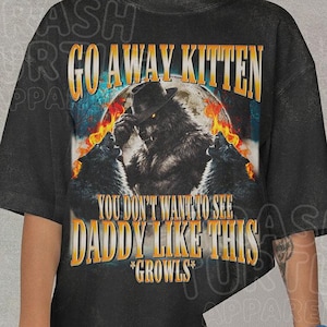Può includere: Una t-shirt nera a maniche corte con una stampa grafica di un lupo con cappello, circondato da fiamme e due lupi che ululano. Il testo recita GO AWAY KITTEN YOU DON'T WANT TO SEE DADDY LIKE THIS *GROWLS* in grassetto giallo e bianco.