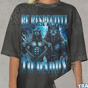 May include: A charcoal gray short-sleeve t-shirt featuring a graphic of two blue-eyed wolves. The text "BE RESPECTFUL" appears above the wolves, and "TO DADDY" is printed below them in a metallic blue font. The design has a distressed aesthetic.