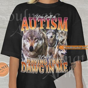 May include: Black t-shirt featuring a wolf pack graphic with the text "You call it AUTISM, I call it HAVING THAT DAWG IN ME." The design includes a gradient orange and yellow color scheme for the text.