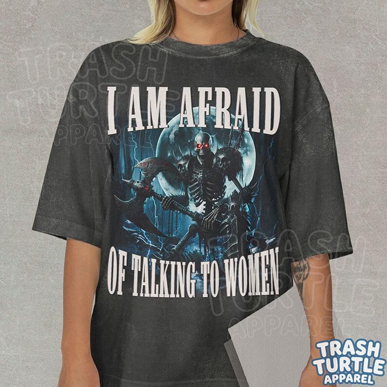May include: A charcoal gray short-sleeve t-shirt featuring a graphic of a skeleton warrior holding an axe in front of a full moon. The text "I AM AFRAID OF TALKING TO WOMEN" is printed in white capital letters above and below the central illustration.