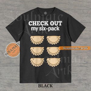 May include: Black t-shirt with the text "CHECK OUT my six-pack" in white. The graphic features six pierogi illustrations in place of a six-pack. The shirt also has the text "SoulmateArtK" and "BLACK" at the bottom.
