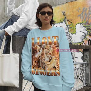 May include: A light blue sweatshirt with a graphic print of multiple orange tabby cats and the text "I LOVE GINGERS".
