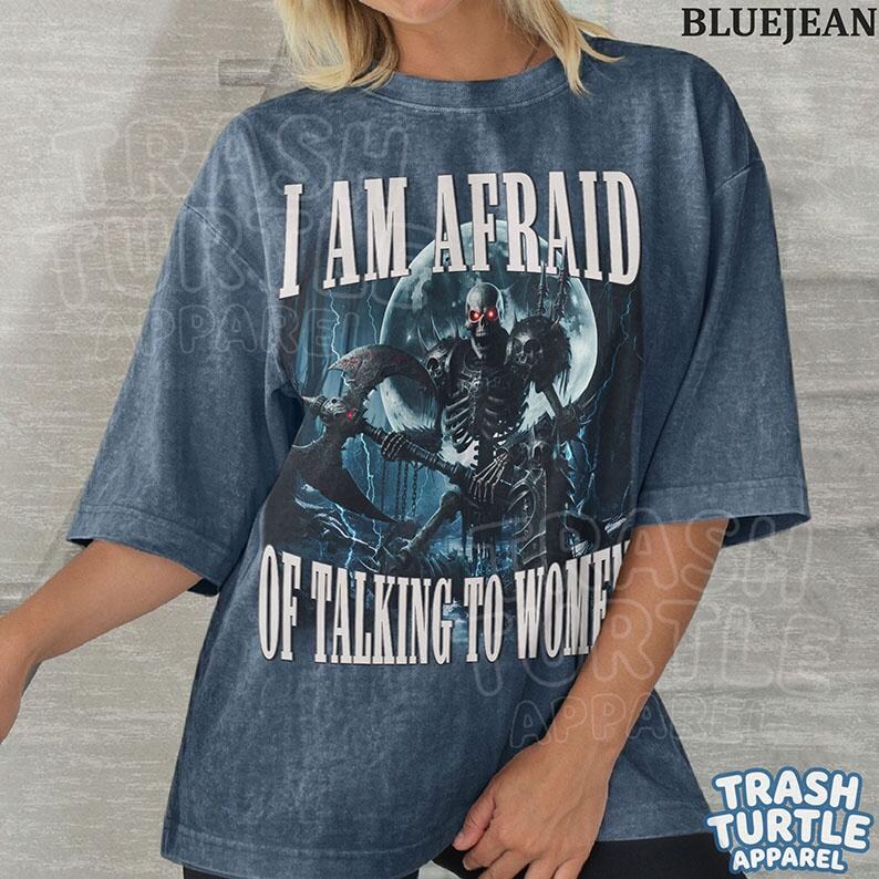 May include: A blue acid-wash t-shirt featuring a graphic of a skeleton holding a large axe in front of a full moon. The text reads I AM AFRAID OF TALKING TO WOMEN in white capital letters. The shirt has short sleeves and a crew neckline.