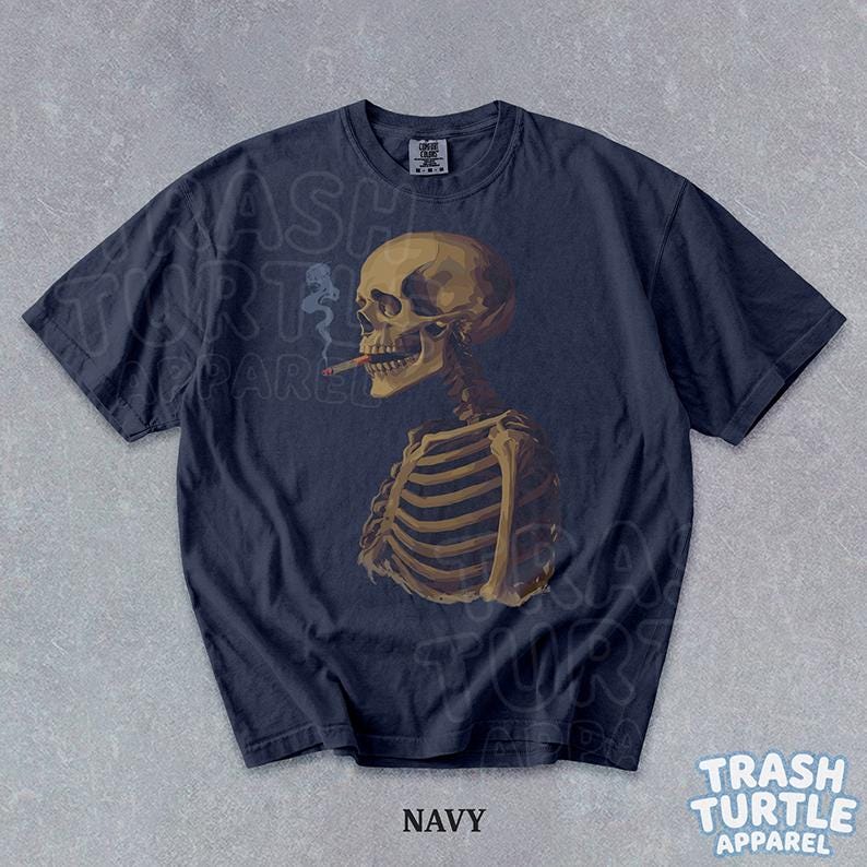 Puede incluir: Camiseta azul marino con una ilustraci&oacute;n detallada de un esqueleto fumando un cigarrillo. El esqueleto se representa de perfil, con detalles anat&oacute;micos. La camiseta tiene el texto "NAVY" en la parte inferior. La marca "TRASH TURTLE APPAREL" tambi&eacute;n es visible.