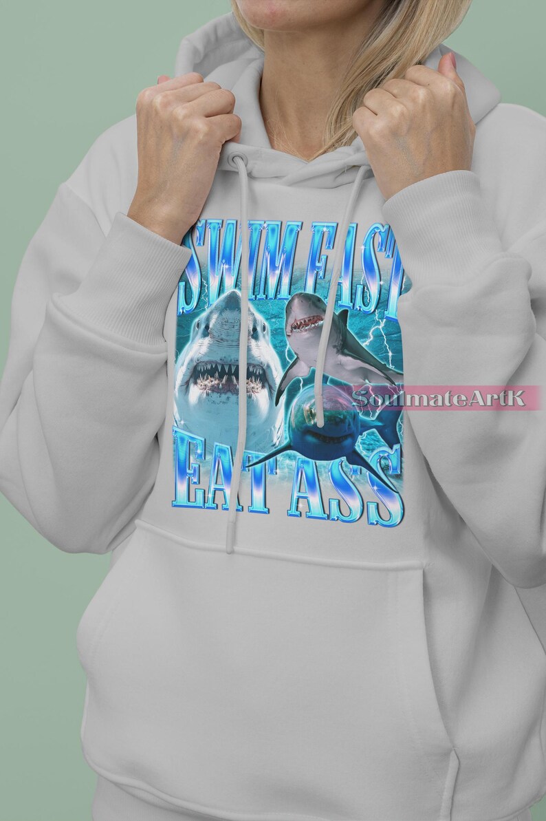 May include: White hoodie featuring a graphic of sharks and the text "SWIM FISH EAT ASS" in blue. The design includes images of sharks with open mouths and a blue background.