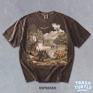 May include: Espresso-colored t-shirt featuring a detailed prehistoric landscape with various dinosaurs, trees, and a volcano. The shirt has a vintage, washed look. The text "ESPRESSO" is printed at the bottom.