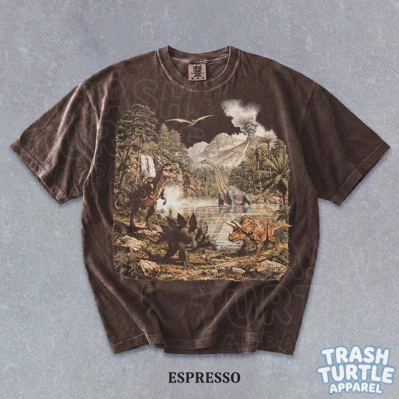 May include: Espresso-colored t-shirt featuring a detailed prehistoric landscape with various dinosaurs, trees, and a volcano. The shirt has a vintage, washed look. The text "ESPRESSO" is printed at the bottom.