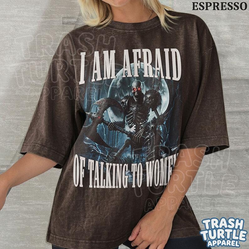 May include: A dark brown, short-sleeved t-shirt featuring a graphic of a skeleton holding an axe in front of a full moon. The text reads I AM AFRAID OF TALKING TO WOMEN in white capital letters. The shirt has a distressed, vintage-style wash.