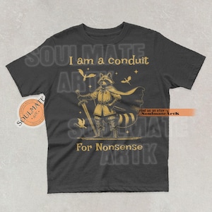 May include: Dark gray t-shirt with a raccoon illustration in a medieval outfit holding a sword. The text "I am a conduit For Nonsense" is printed in gold. The shirt has a round neck and short sleeves.
