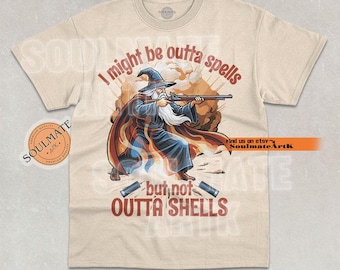 Op de afbeelding: Beige t-shirt met een afbeelding van een tovenaar die met een geweer richt, met de tekst "I might be outta spells but not OUTTA SHELLS." De tovenaar draagt een blauwe mantel en hoed, met een witte baard. Twee hulzen liggen onderaan.