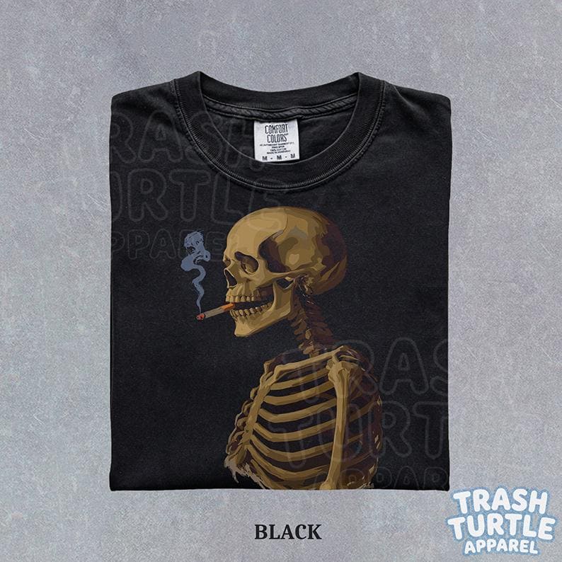 Puede incluir: Camiseta negra con una ilustraci&oacute;n detallada de un esqueleto fumando un cigarrillo. El esqueleto est&aacute; representado de perfil, con un cr&aacute;neo y una caja tor&aacute;cica. La camiseta tiene el texto "BLACK" en la parte inferior y la marca "TRASH TURTLE APPAREL".