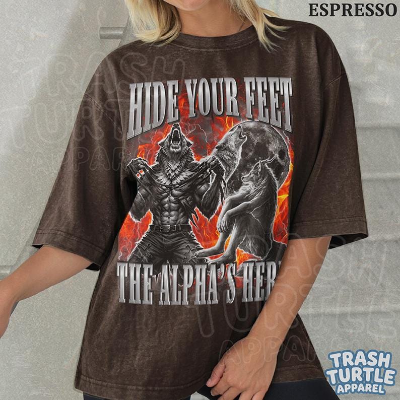 May include: Espresso-colored t-shirt featuring a werewolf graphic with the text "HIDE YOUR FEET" and "THE ALPHA'S HERE". The design includes a full moon and flames. The shirt is from Trash Turtle Apparel.
