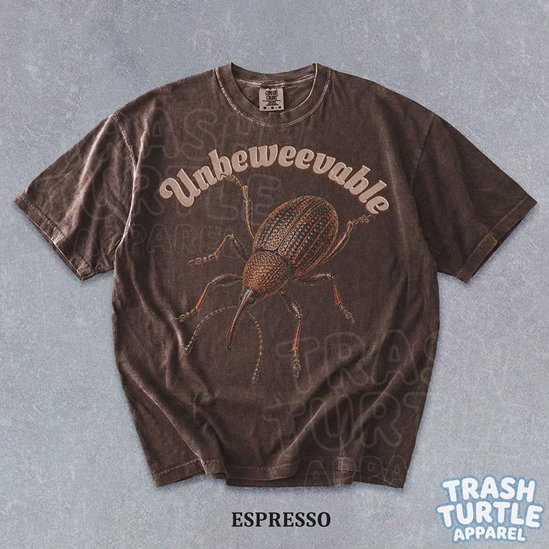 Puede incluir: Una camiseta de manga corta de color marr&oacute;n oscuro con un gr&aacute;fico de un gorgojo en el centro. El texto "Unbeweevable" est&aacute; impreso en una fuente clara y curva sobre el insecto. La camiseta tiene cuello redondo y un acabado desgastado.