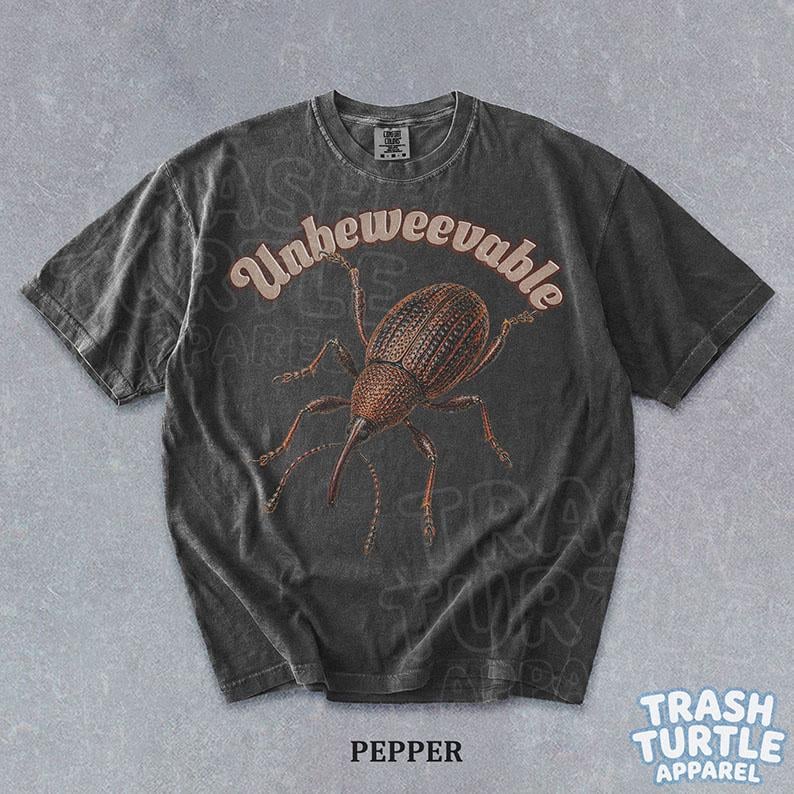 Puede incluir: Una camiseta de manga corta gris carb&oacute;n con una ilustraci&oacute;n marr&oacute;n de un insecto gorgojo centrada en el pecho. Sobre el insecto, la palabra Unbeweevable est&aacute; impresa en una fuente curva de color claro. La camiseta tiene cuello redondo.