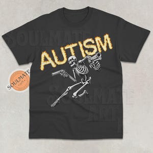 Op de afbeelding: Zwart T-shirt met een skelet dat twee pistolen vasthoudt en het woord "AUTISME" in vlammen erboven.