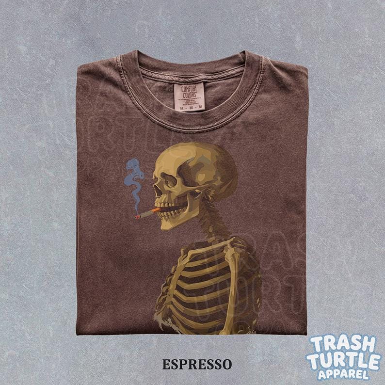 Puede incluir: Camiseta color espresso con una ilustraci&oacute;n detallada de un esqueleto fumando un cigarrillo con humo azul. La camiseta tiene cuello redondo y una etiqueta que dice "Comfort Colors". El texto "ESPRESSO" est&aacute; en la parte inferior.