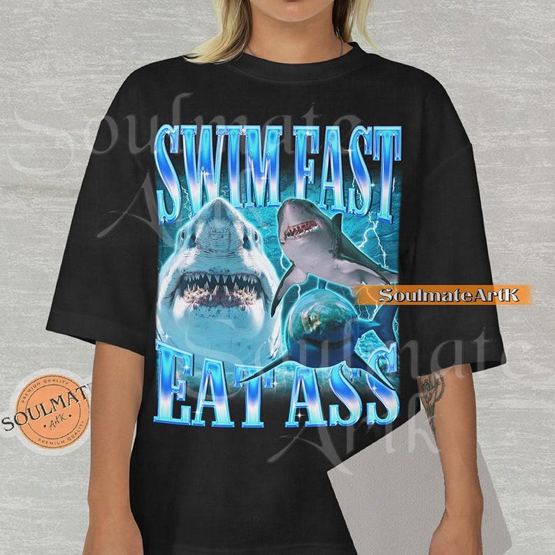 May include: Black t-shirt featuring a graphic design with three sharks and the text "SWIM FAST EAT ASS" in blue. The design includes lightning bolts and a distressed font. The shirt has a round neck and short sleeves.