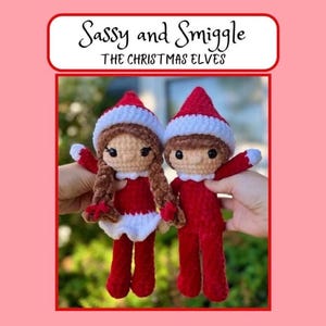 Op de afbeelding: Twee gehaakte poppen, Sassy en Smiggle, de kerstelfjes. Elke pop draagt een rood-witte muts en een rode outfit. De ene pop heeft bruin garen haar in vlechten, de andere heeft kort bruin haar. Beide hebben zwarte ogen en een lichte huid.