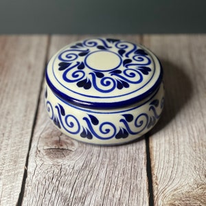 May include: A white ceramic trinket box with a blue and white floral design. The lid is closed.
