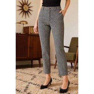 Può includere: Pantaloni a vita alta con motivo pied-de-poule bianco e nero. I pantaloni presentano un taglio dritto, chiusura con bottone e cerniera in vita e una finitura in tessuto testurizzato. Il design include passanti per cintura e tasche.
