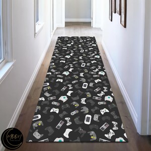 Könnte beinhalten: Ein schwarz-weißer Läuferteppich mit einem sich wiederholenden Muster von Videospielcontrollern. Der Teppich liegt in einem Flur mit weißen Wänden und einem Holzboden.