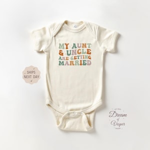May include: Cream-colored baby bodysuit with the text "MY AUNT & UNCLE ARE GETTING MARRIED" in retro-style lettering. The text is in shades of green, orange, and purple. The bodysuit has short sleeves and a snap closure.