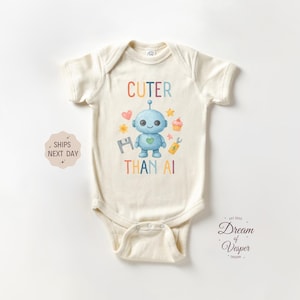 May include: Cream-colored baby bodysuit with a colorful robot graphic and the text "Cuter Than AI." The robot is light blue with a heart-shaped chest and is surrounded by hearts, stars, and a cupcake. A cute baby outfit.